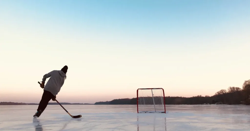 Single hockey player on a frozen lake heading toward a goal. The sun is setting in the background.